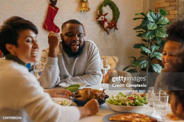 happy young african american family of father, mother and two daughters enjoying christmas lunch of turkey and pizza at decorated house celebrating xmas and new years eve - 40 44 years 個照片及圖片檔