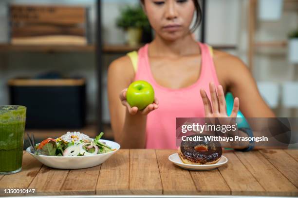 young girl on dieting for good health concept. close up female using hand reject junk food by pushing out her favorite donuts and choose red apple and salad for good health - carbohidrato fotografías e imágenes de stock