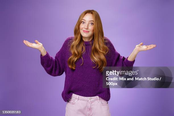 portrait of young woman standing against purple background - schulterzucken stock-fotos und bilder