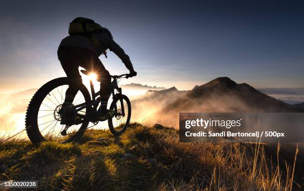 silhouette of man riding bicycle on mountain against sky during sunset,planina pod golico,slovenia - cyclist mountain stock pictures, royalty-free photos & images
