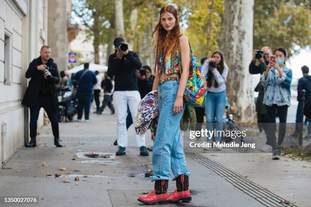 Model Clementine Balcaen wears a vintage print vest, blue floral print mesh backpack, blue jeans, and red and brown cowboy Western boots after the...