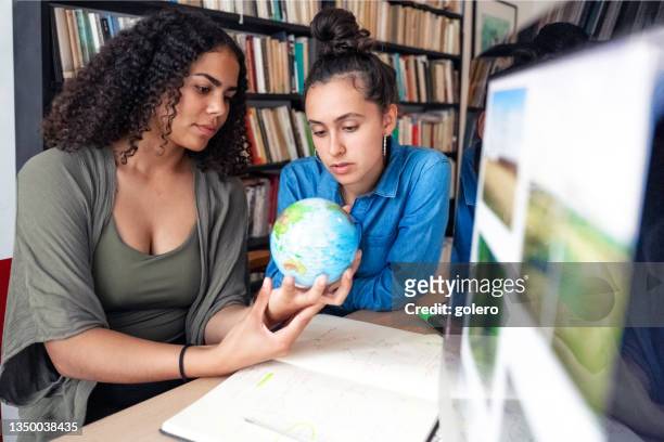 two young woman looking together on globe for studies - 地圖學 個照片及圖片檔
