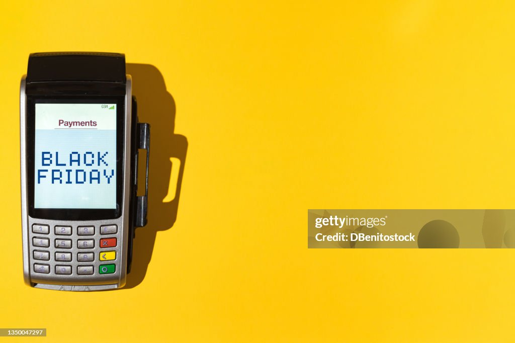 Dataphone with the word 'Black Friday' on the screen on yellow background at the left side. Black friday, shopping, commerce and credit cards concept.