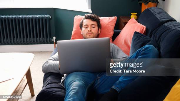 young man using laptop and lying on sofa - couch potato expressão em inglês - fotografias e filmes do acervo