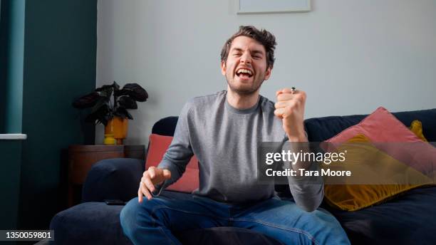 man celebrating on sofa in house - celebrating in sofa stock pictures, royalty-free photos & images