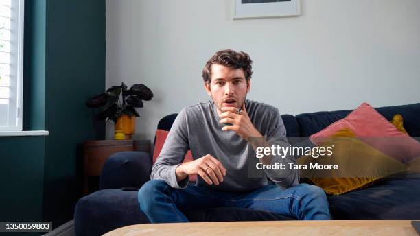 young man looking shocked on sofa - one man only stock pictures, royalty-free photos & images