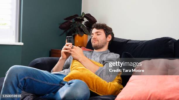 man sitting on sofa looking at smart phone - générique photos et images de collection