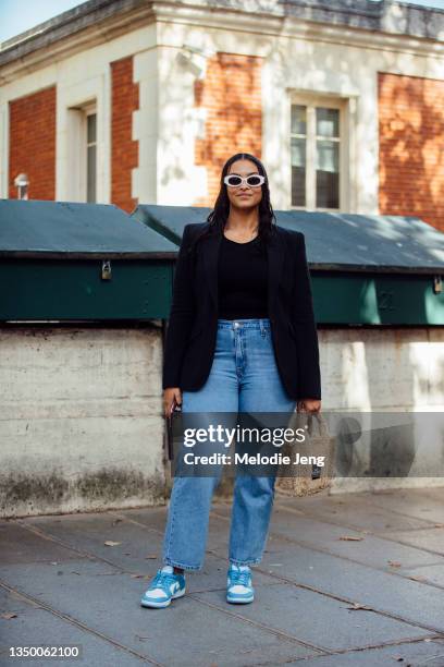 Model Devyn Garcia wears tan Kurt Cobain-style sunglasses, a black blazer, black top, blue jeans, blue and white Nike sneakers, and tan Marc Jacobs...