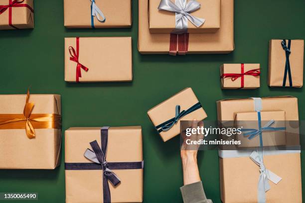 persona anónima sosteniendo una de las muchas cajas de regalo sobre un fondo verde - gift fotografías e imágenes de stock