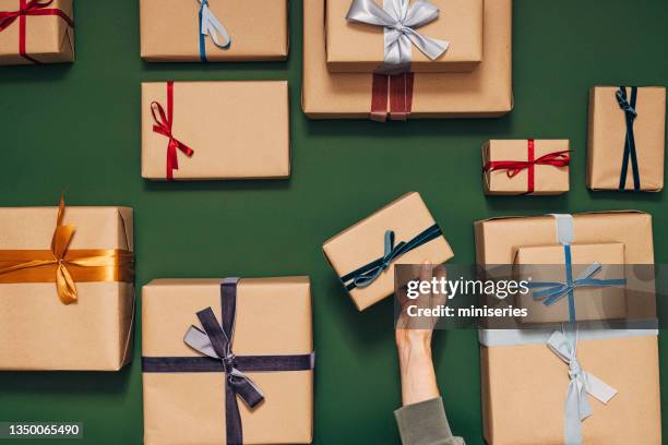 anonymous person holding one of many gift boxes on a green background - hand with gift stock pictures, royalty-free photos & images