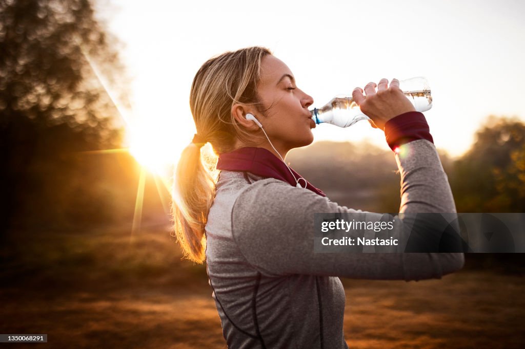 Junge fitte Frau, die bei Sonnenaufgang eine Pause vom Joggen in der Natur einlegen kann