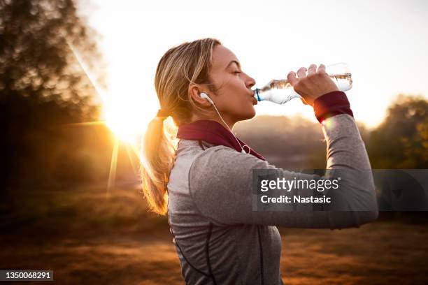 giovane donna in forma che si prende una pausa dal jogging nella natura durante l'alba - acqua potabile foto e immagini stock