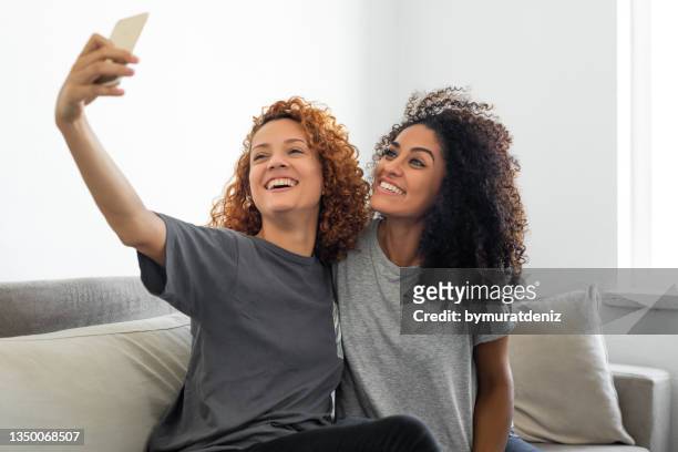 beautiful women sitting together at home taking selfie with mobile phone - cool couple in apartment stock pictures, royalty-free photos & images