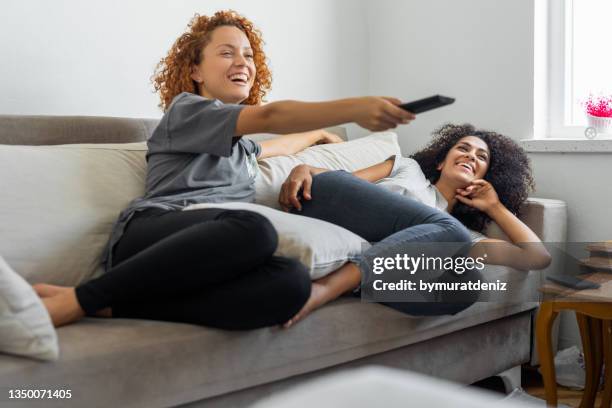 le amiche stanno guardando il loro programma televisivo preferito mentre sono sedute sul divano - channel foto e immagini stock