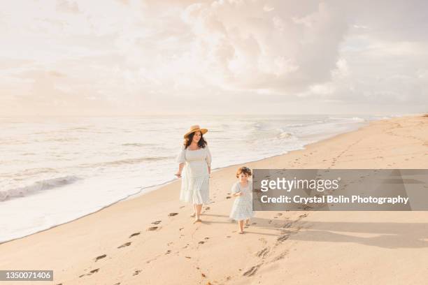 a 7 months pregnant mother & 2-year-old daughter enjoying time together on the beach during a golden sunrise on palm beach, florida - beach florida family stockfoto's en -beelden