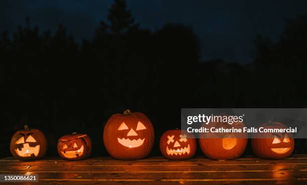 a row of various sized carved hallowe'en pumpkins with different facial expressions glowing in the dark. space for copy. - halloween stockfoto's en -beelden