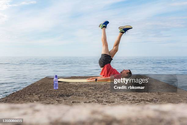 athletic guy lying on a exercise mat performs leg up exercises to train core muscles - side lying leg lift stock pictures, royalty-free photos & images