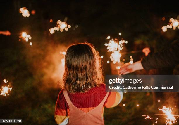 a child holds a sparkler in the darkness, surrounded by other burning sparklers - family fireworks stockfoto's en -beelden