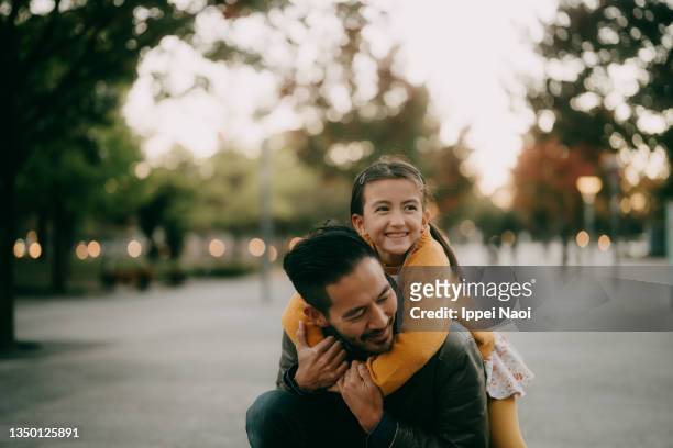 young girl hugging her father from behind at dusk - padre soltero fotografías e imágenes de stock