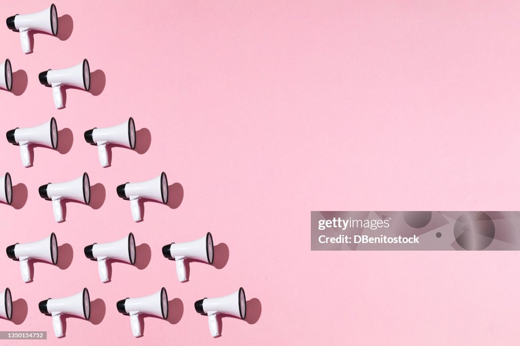 White megaphones pattern with black ornament on pink background on the left side, with copy space. Shout, message, announcement and news concept.