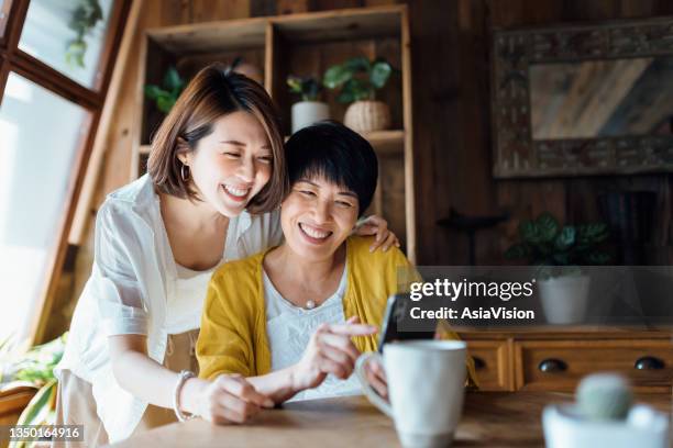 cariñosa madre e hija asiáticas mayores usando teléfonos inteligentes juntos en casa, sonriendo alegremente, disfrutando del tiempo de unión de madre e hija. familia y tecnología multigeneración - fitness instructor fotografías e imágenes de stock