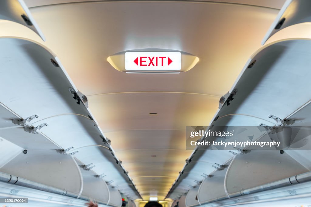 Emergency exit sign on ceiling inside passenger aircraft cabin