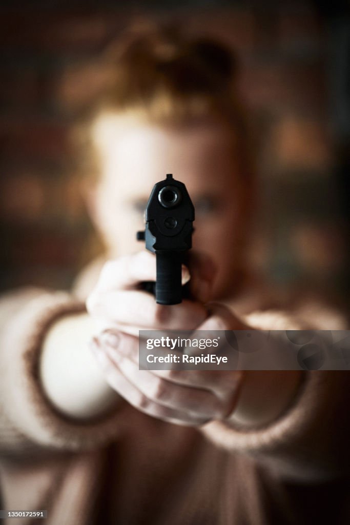 Young redhead woman taking aim at the camera with a gun