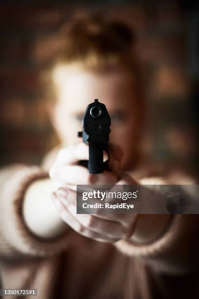 young redhead woman taking aim at the camera with a gun - pistool handwapen stockfoto's en -beelden