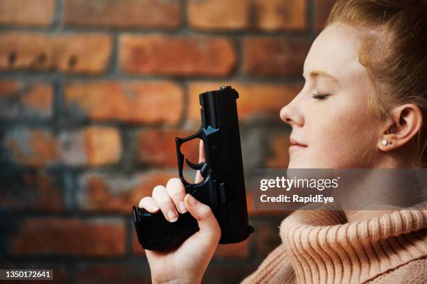 young redhead woman holding a gun and looking serene, with her eyes closed - hand holding gun stockfoto's en -beelden