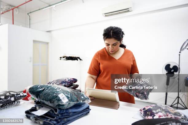 woman using a tablet to fulfill clothing orders in a warehouse - plus size fashion stock pictures, royalty-free photos & images