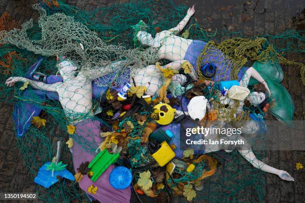 Activists from the environmental group Ocean Rebellion lie caught in a deep sea fishing net trailed behind a sculpture of a bottom trawling fishing...