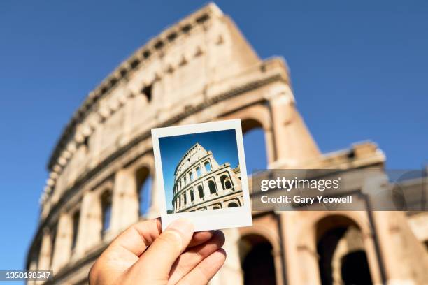 man holding instant film photo in front of the colosseum at sunset - colosseum stock pictures, royalty-free photos & images