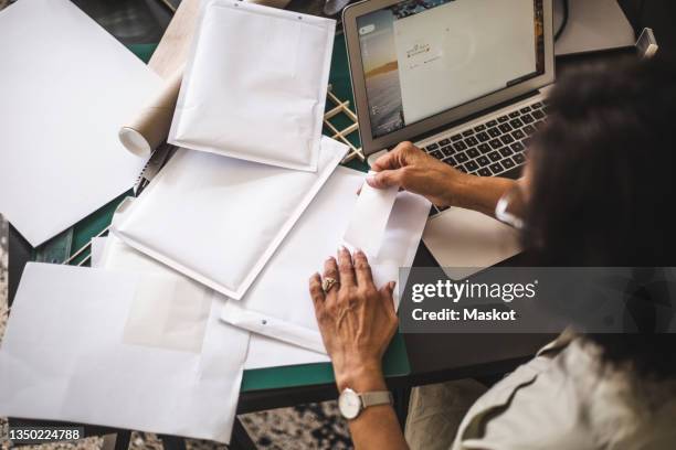 high angle view of female owner labeling on envelope while working in office - high sticking stock pictures, royalty-free photos & images