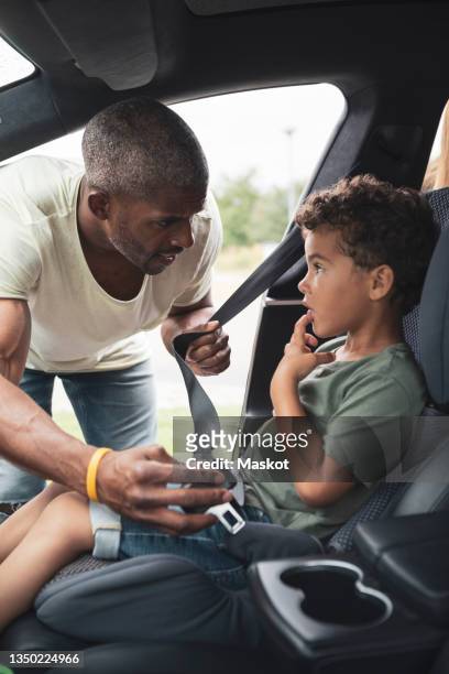father talking with son while fastening seat belt in car - fastening stock-fotos und bilder