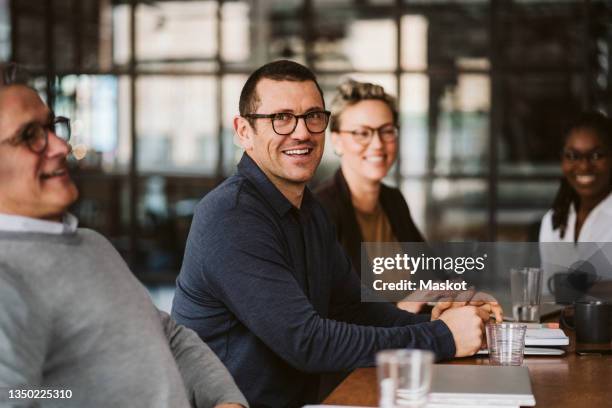 portrait of mid adult businessman sitting amidst colleagues at conference table - blick in die kamera stock-fotos und bilder