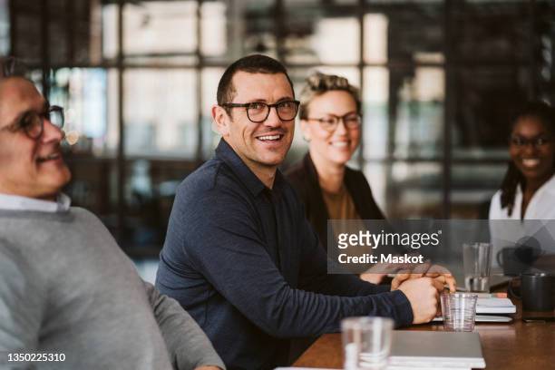 portrait of mid adult businessman sitting amidst colleagues at conference table - men meeting ストックフォトと画像