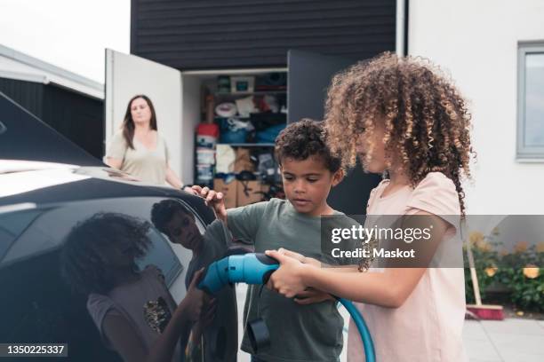 sister and brother charging electric car at front yard - car yard stock-fotos und bilder