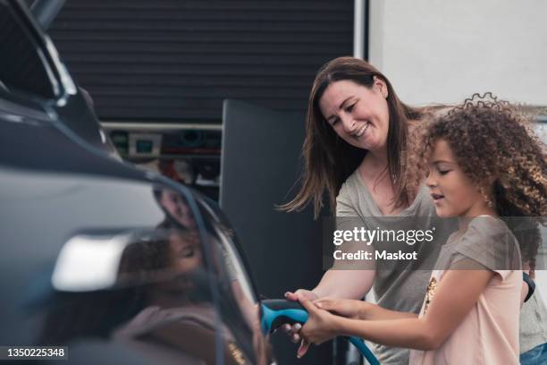 smiling mother assisting daughter in charging electric car at front yard - electric car home stock pictures, royalty-free photos & images