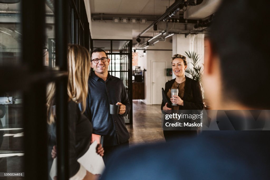 Businessmen and businesswomen discussing while standing at corridor in office