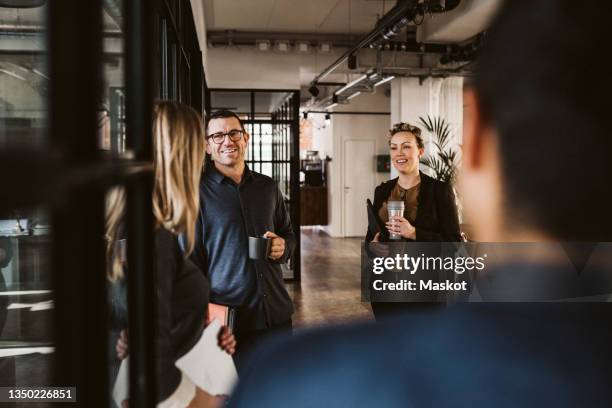 businessmen and businesswomen discussing while standing at corridor in office - employee engagement stock pictures, royalty-free photos & images