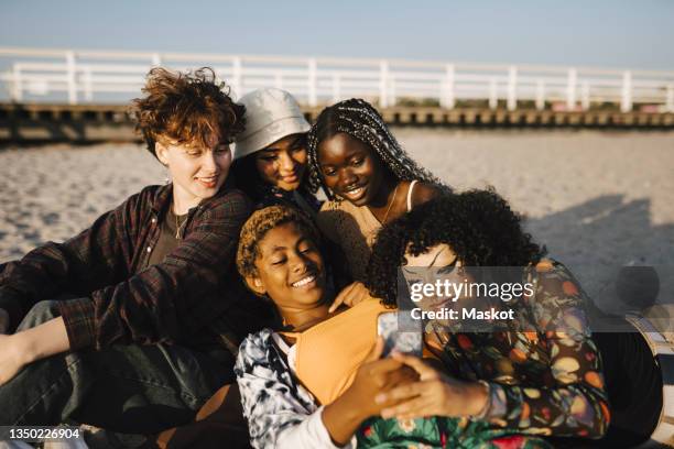 smiling multiracial friends with mobile phone at beach - boys mobile phone group stock-fotos und bilder