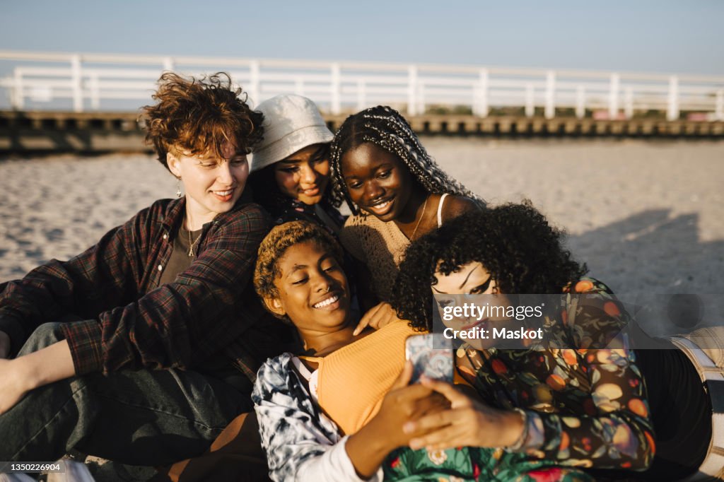 Smiling multiracial friends with mobile phone at beach