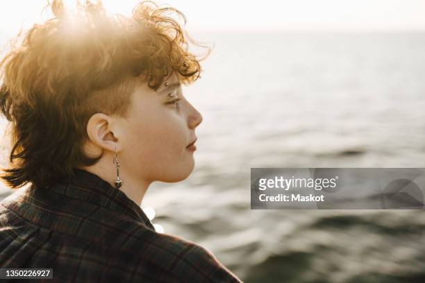 teenage boy with piercing looking at sea - transgender stock-fotos und bilder