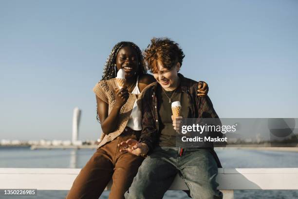 teenage boy and young woman holding ice cream while sitting on railing - 18 stock-fotos und bilder