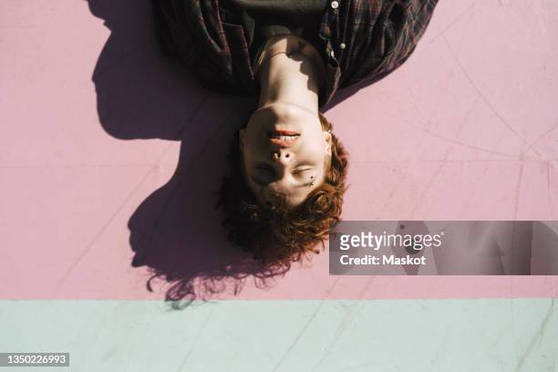 teenage boy with eyes closed lying on pink footpath during sunny day - transa stock-fotos und bilder