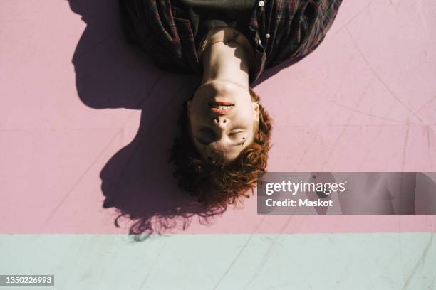 teenage boy with eyes closed lying on pink footpath during sunny day - boy floor stockfoto's en -beelden