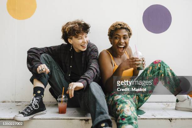 cheerful friends sitting with drinks on retaining wall - teen boys stock-fotos und bilder