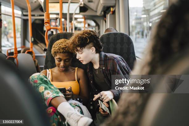 teenage boy looking at young non-binary woman using smart phone in bus - lgbtqi people fotografías e imágenes de stock