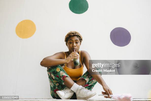 young non-binary person having drink against polka dots on wall - 非二元性別 個照片及圖片檔