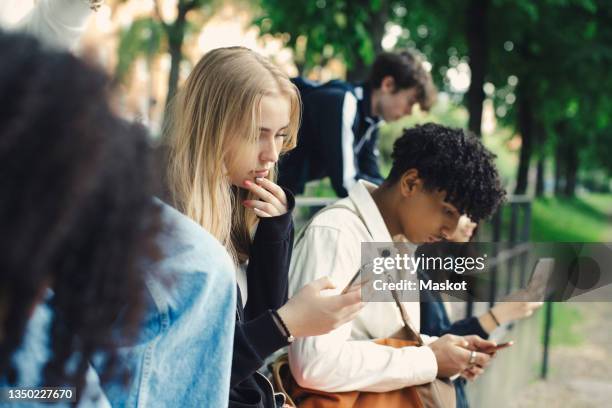 male and female friends using smart phones in park - social networking foto e immagini stock